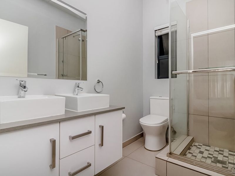 Modern bathroom featuring a double vanity with white cabinetry, a glass-enclosed shower with tiled flooring, and neutral wall finishes.