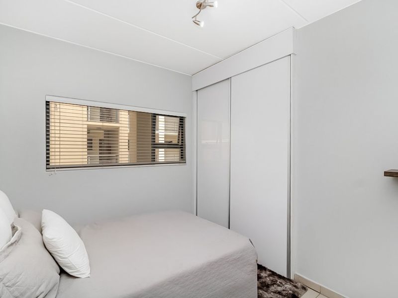 A clean and modern bedroom featuring a built-in sliding door wardrobe, neutral wall finishes, and a functional floating shelf.