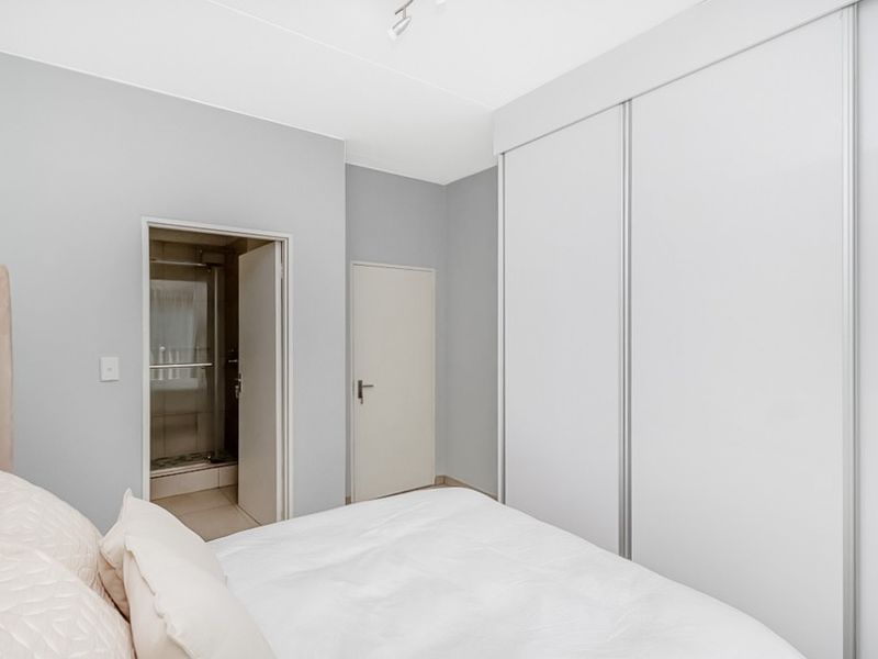 A clean, modern bedroom featuring built-in sliding door wardrobes and direct access to an en-suite bathroom.
