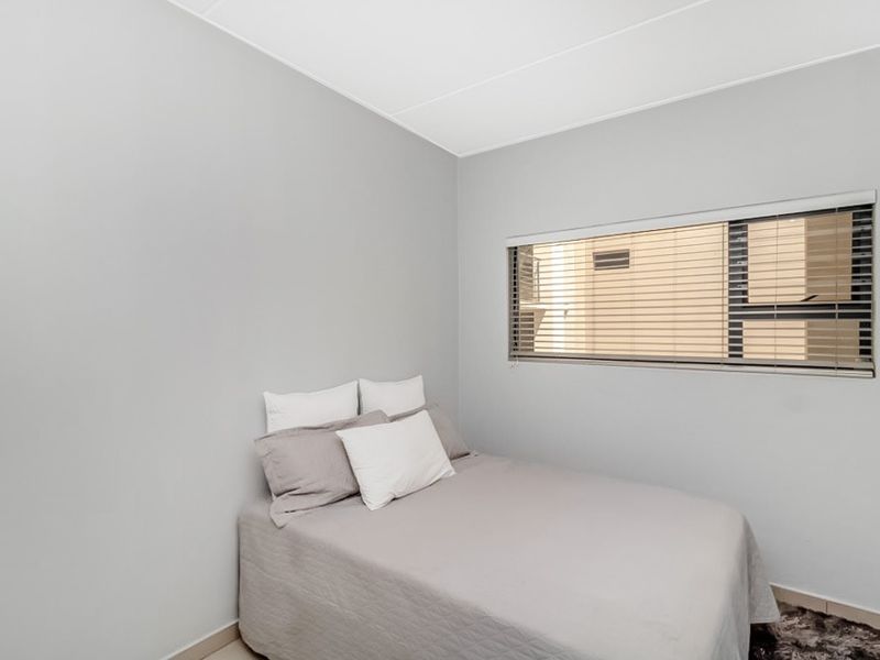 A clean and neutral bedroom featuring a horizontal window with fitted venetian blinds, providing natural light and a simple, modern aesthetic.