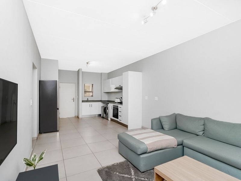 Modern open-plan living area featuring a sleek kitchen with built-in cabinetry, integrated appliances, and neutral tiled flooring throughout the space.