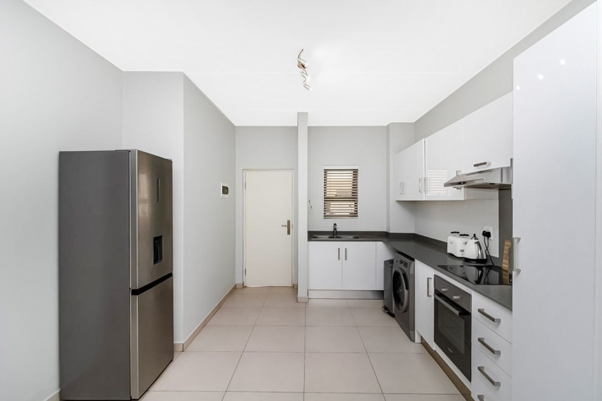Modern kitchen featuring sleek white cabinetry, dark countertops, integrated oven, hob, extractor fan, and dedicated space for laundry appliances.