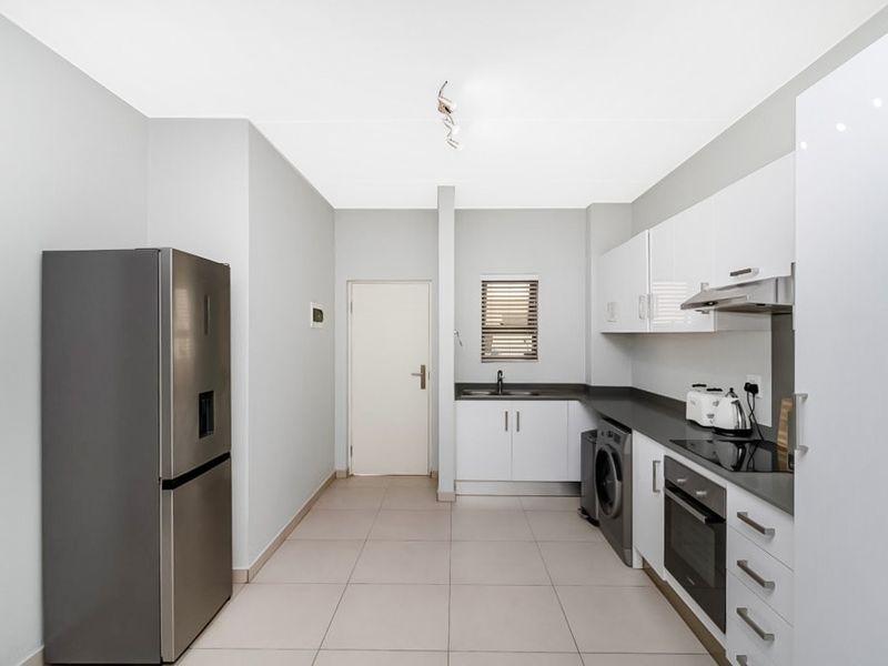 Modern kitchen featuring sleek white cabinetry, dark countertops, integrated oven, hob, extractor fan, and dedicated space for laundry appliances.