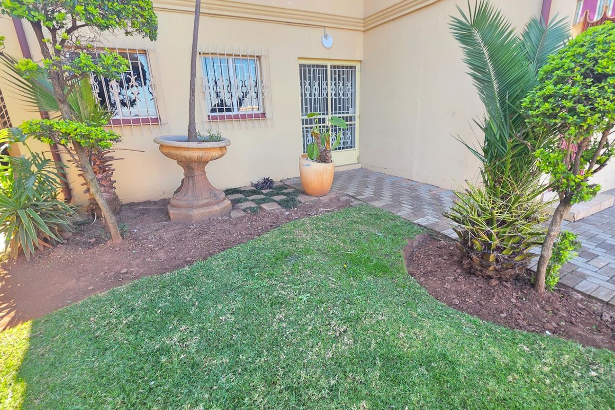 A rear exterior view of the apartment featuring a small lawn, paved walkway, and security bars on the windows.