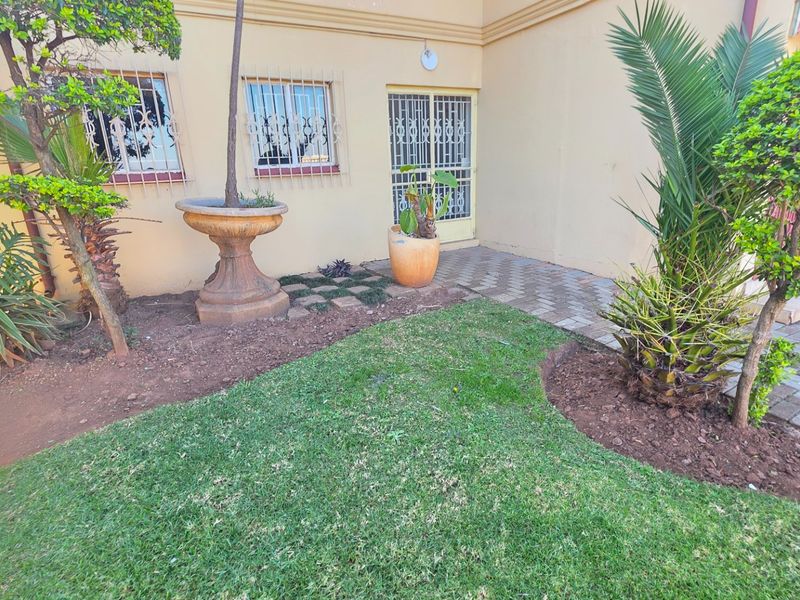 A rear exterior view of the apartment featuring a small lawn, paved walkway, and security bars on the windows.