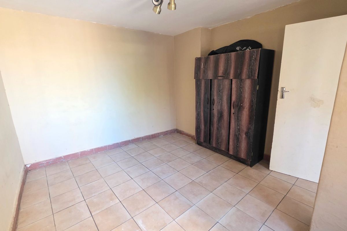 A simple bedroom featuring tiled flooring and neutral wall finishes, offering a blank canvas for potential updates or interior design improvements.