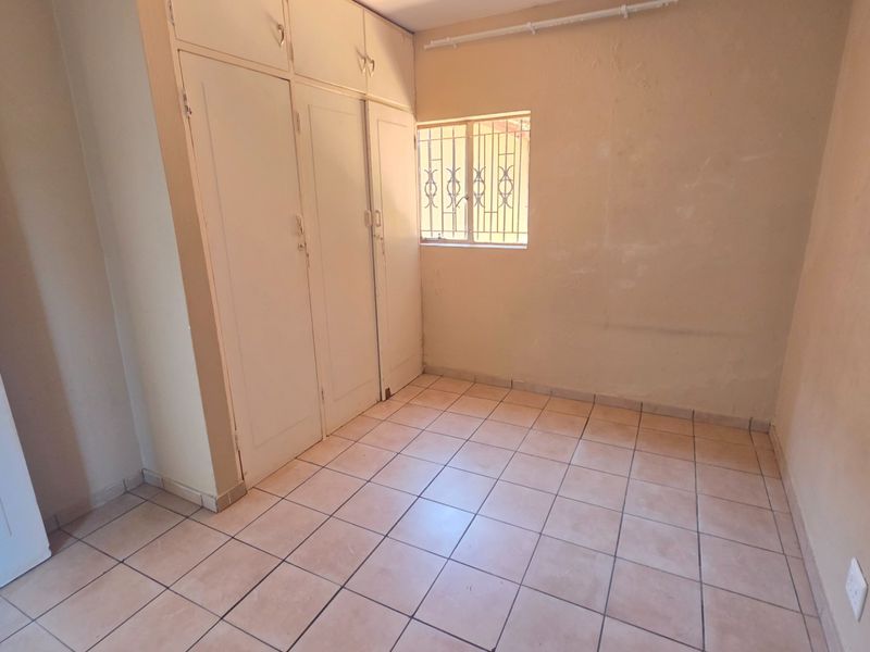An empty bedroom featuring tiled flooring, built-in cupboards, and a window with security bars, offering a blank canvas for renovation.