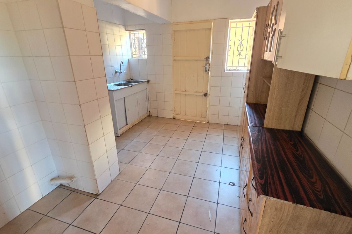 A dated kitchen featuring tiled surfaces, built-in cabinetry, and a double sink, offering a blank canvas for renovation and modernization.