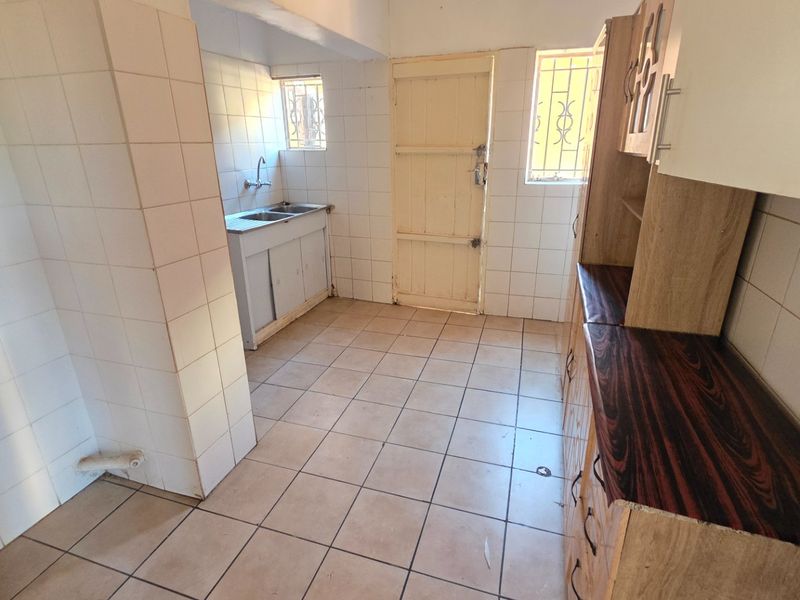 A dated kitchen featuring tiled surfaces, built-in cabinetry, and a double sink, offering a blank canvas for renovation and modernization.