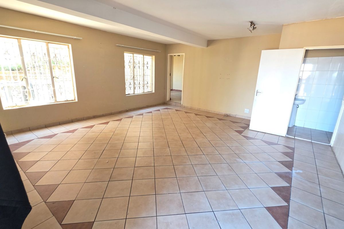 An empty, open-plan living area featuring ceramic floor tiles, security bars on windows, and direct access to an adjacent bathroom.