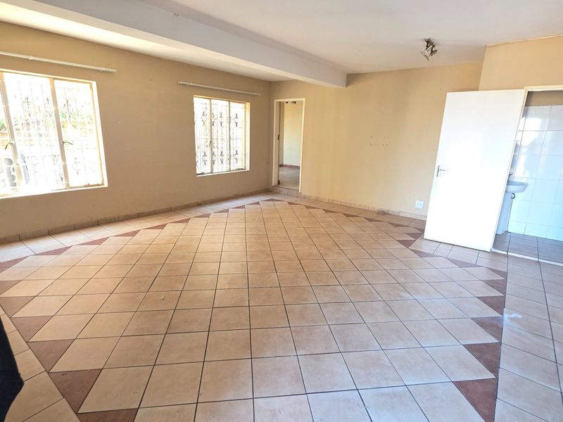 An empty, open-plan living area featuring ceramic floor tiles, security bars on windows, and direct access to an adjacent bathroom.