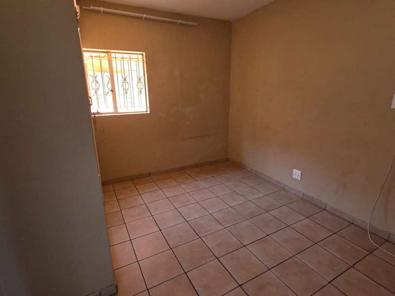 An empty bedroom featuring tiled flooring, a window with security bars, and neutral wall finishes, ready for a fresh coat of paint.