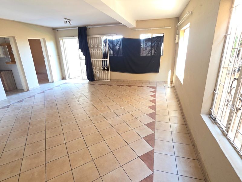 Spacious open-plan living area featuring tiled flooring, security gates, and burglar bars, offering a blank canvas for renovation and interior design.