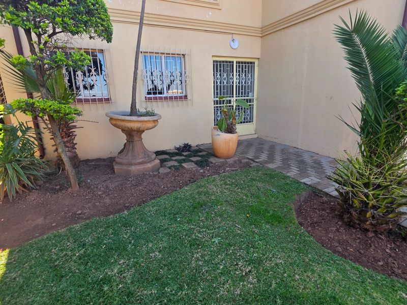 A rear exterior view of the apartment featuring a small lawn, paved walkway, and security bars on the windows and door.