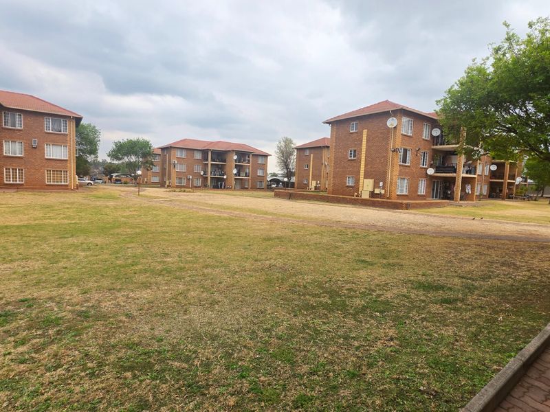 A view of the apartment complex exterior featuring brick buildings, tiled roofs, and shared communal garden spaces.