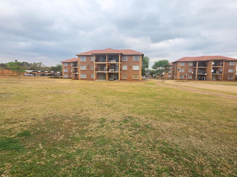 Exterior view of a multi-story brick apartment complex featuring private balconies and a large, open communal lawn area.