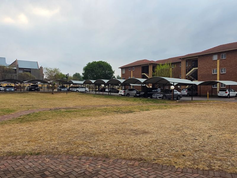 Exterior view of an apartment complex featuring multiple covered parking bays and a large open lawn area.