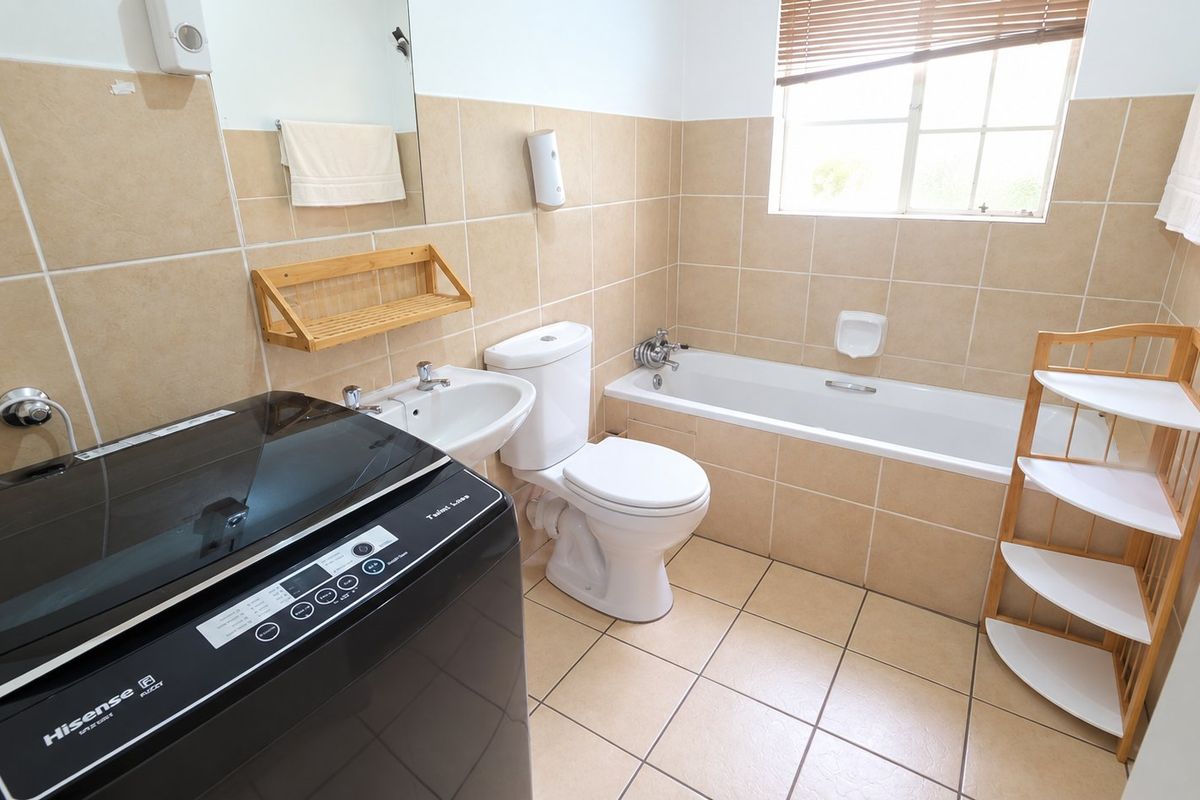A functional bathroom featuring a bathtub, toilet, and washbasin with neutral wall and floor tiling, providing a clean and practical space.