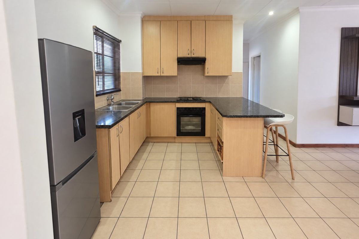 A functional kitchen featuring light wood cabinetry, granite countertops, built-in oven, hob, and tiled flooring, offering a clean and practical workspace.
