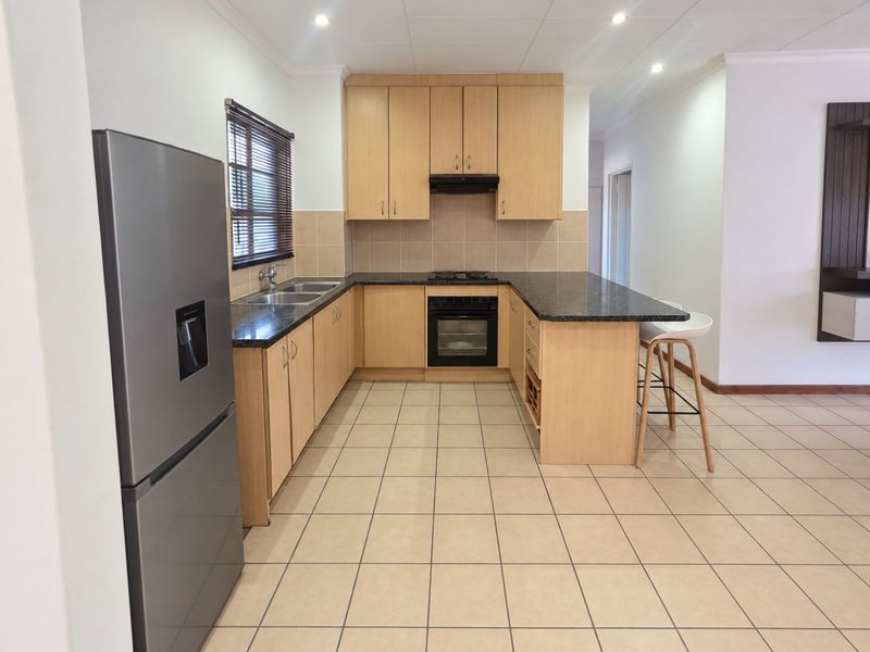 A functional kitchen featuring light wood cabinetry, granite countertops, built-in oven, hob, and tiled flooring, offering a clean and practical workspace.