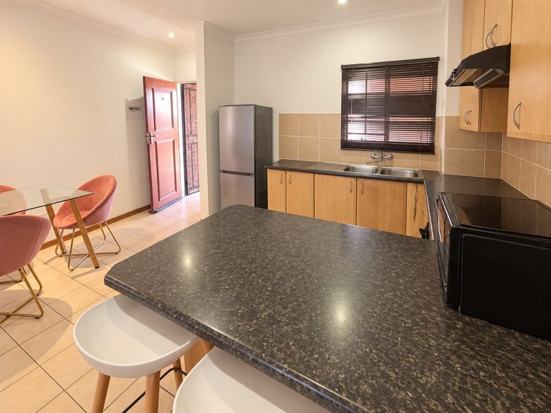 Open-plan kitchen and dining area featuring laminate cabinetry, dark countertops, tiled flooring, and direct access to the entrance.