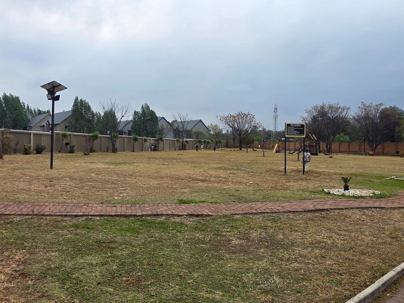 A large communal garden area featuring a paved walkway, perimeter walling, and basic playground equipment within an apartment complex.