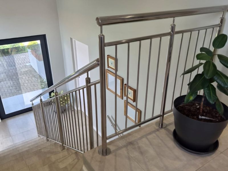 A bright, modern staircase landing featuring a stainless steel balustrade, neutral tiled flooring, and a large glass door providing natural light.