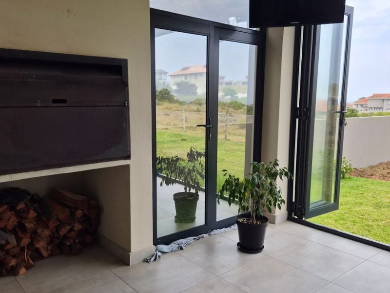 Covered patio area featuring a built-in braai, large format floor tiles, and aluminium stack doors opening to the garden.