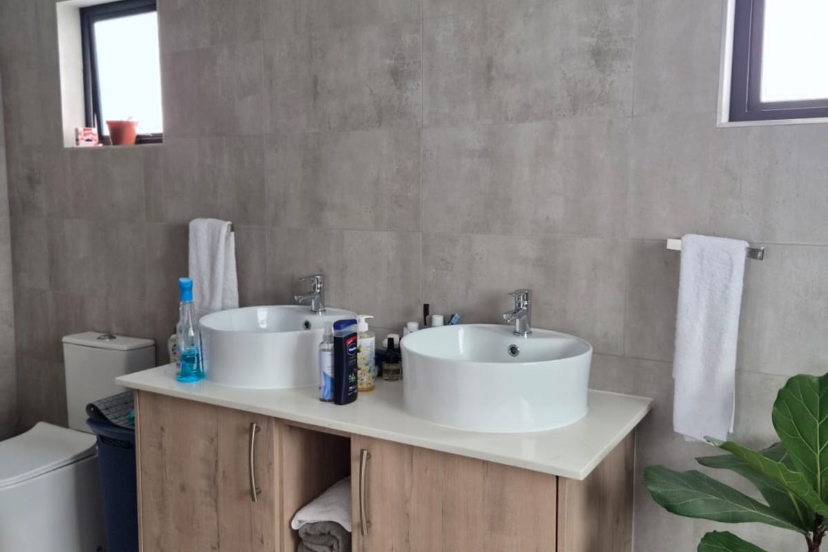 Modern bathroom featuring a double vanity with vessel sinks, wood-finish cabinetry, and neutral grey wall and floor tiling.