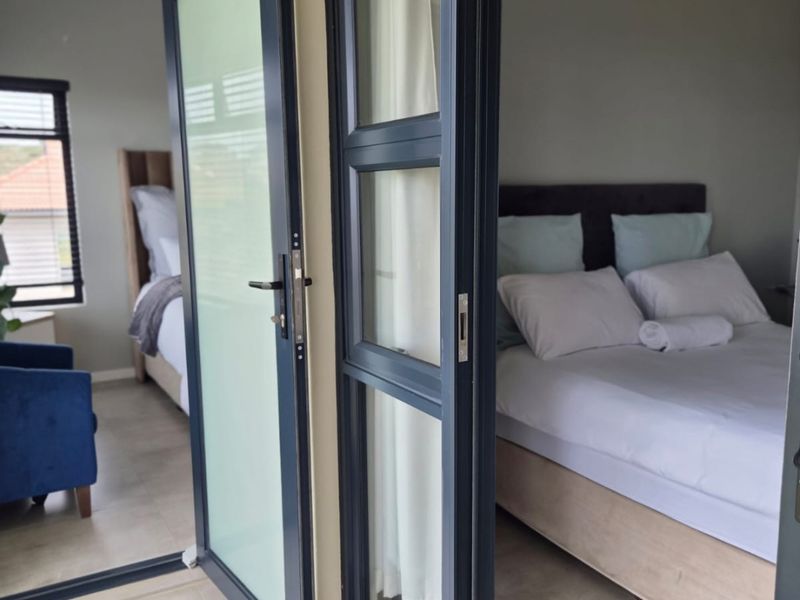 A view into a bedroom featuring modern aluminium framed glass doors and neutral tiled flooring, providing a clean and contemporary aesthetic.