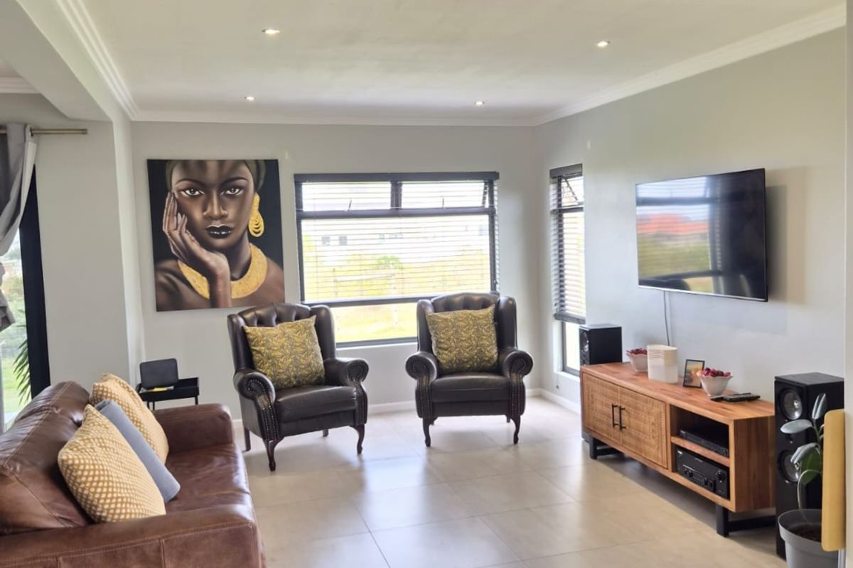 A bright and spacious living room featuring neutral tiled flooring, recessed downlighting, and large aluminium-framed windows with modern blinds.