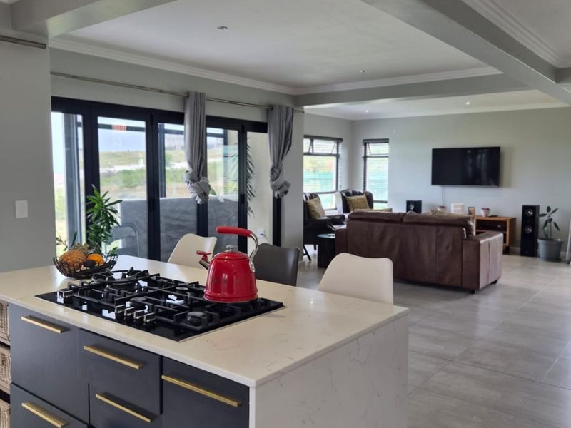 Spacious open-plan living area featuring a modern kitchen island with gas hob, quartz countertops, and seamless flow to the lounge with large sliding doors.