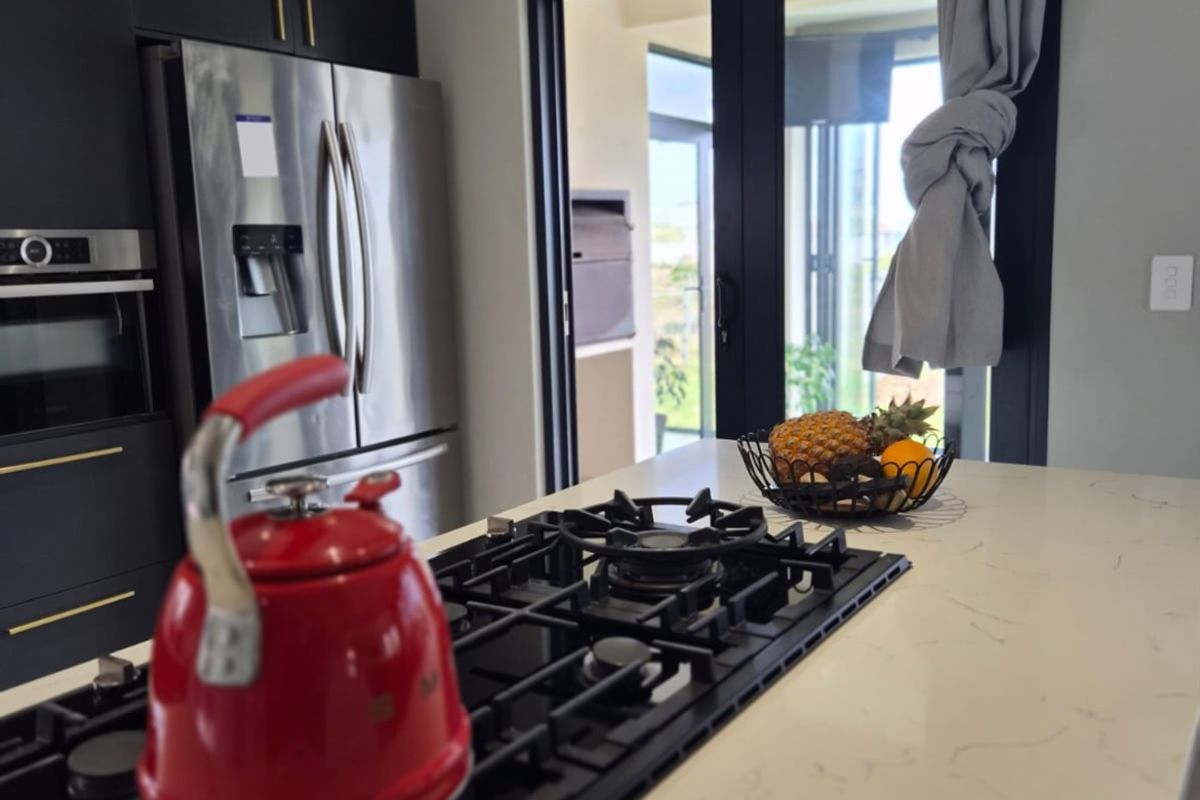 Modern kitchen featuring a central island with a gas cooktop, stone countertops, sleek black cabinetry, and direct access to an outdoor patio area.