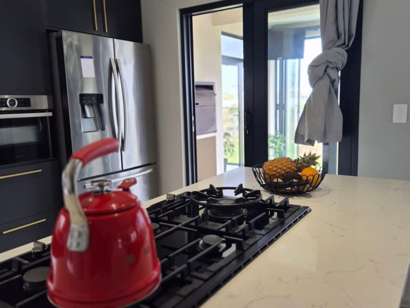 Modern kitchen featuring a central island with a gas cooktop, stone countertops, sleek black cabinetry, and direct access to an outdoor patio area.
