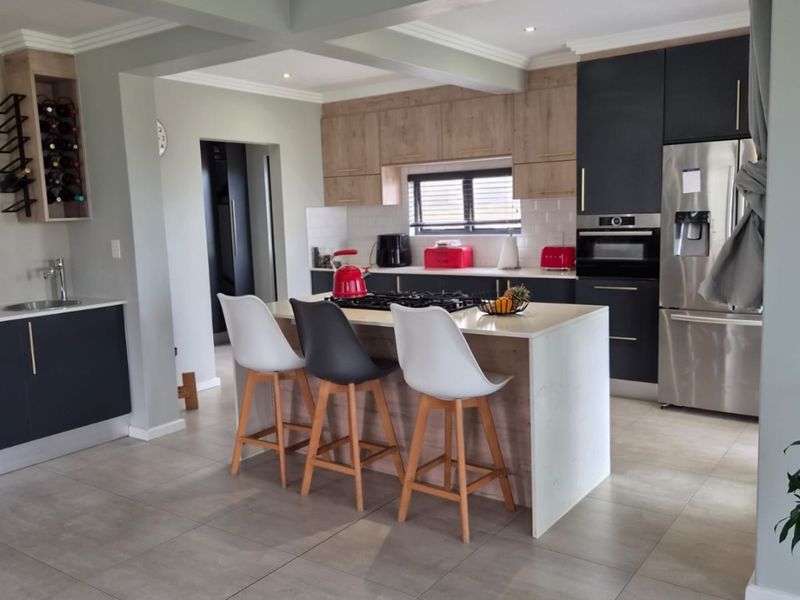 Modern open-plan kitchen featuring a central island with stone countertops, dark and wood-tone cabinetry, built-in appliances, and sleek tiled flooring.