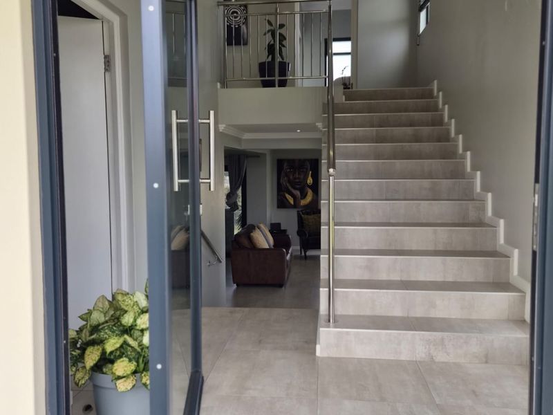 Welcoming entrance hall featuring modern tiled flooring, a sleek staircase with stainless steel balustrade, and recessed lighting, leading into the main living area.
