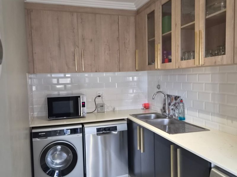 A modern, well-appointed scullery featuring sleek two-tone cabinetry, subway tile backsplash, quartz countertops, and integrated space for laundry and dishwashing appliances.