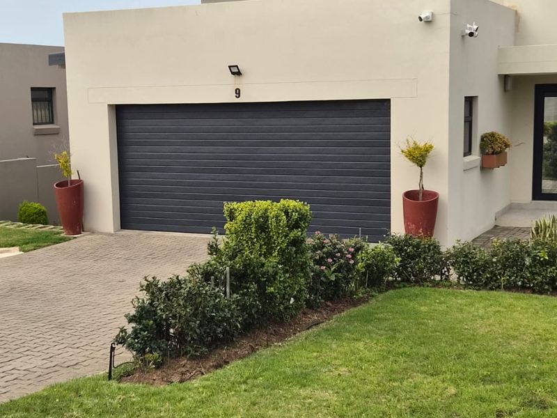 Front elevation of a modern residence featuring a paved driveway, a dark automated garage door, and well-maintained landscaping.