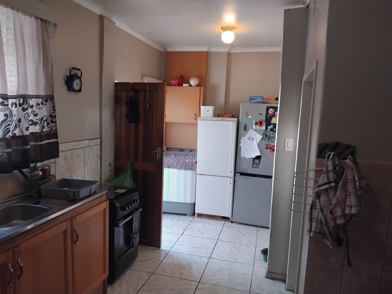 A functional kitchen featuring wooden cabinetry, tiled flooring, and a tiled splashback, offering a practical layout with space for essential appliances.