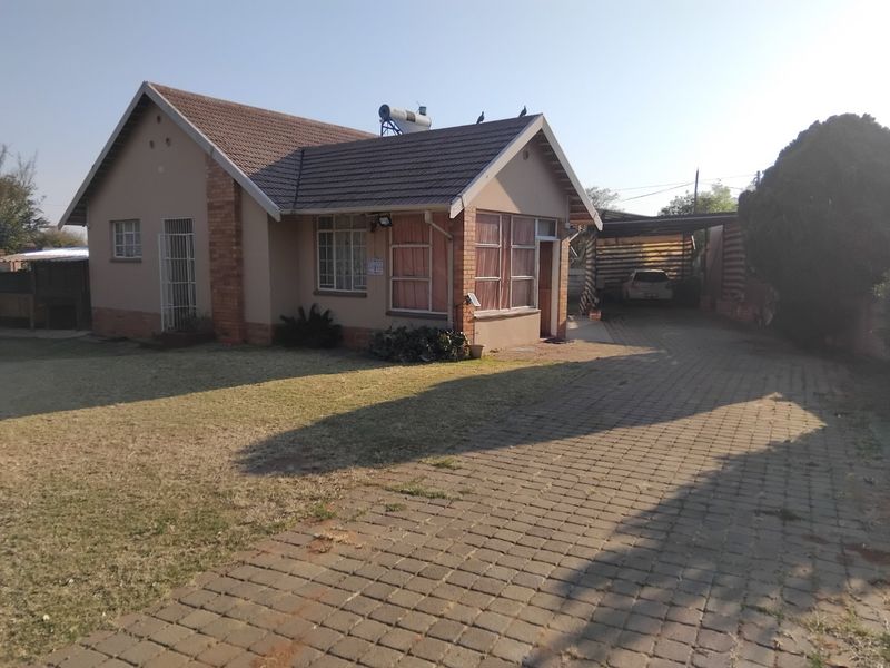 Front view of a single-story house featuring a tiled roof, solar geyser, brick driveway, and a covered carport area.