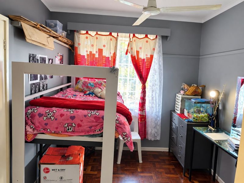 A bedroom featuring parquet flooring, a ceiling fan, and a window with security bars, offering a functional space with potential for cosmetic updates.