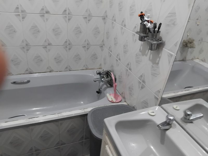 A functional bathroom featuring a grey bathtub, wall-mounted mixer tap, and tiled walls with a vanity basin and mirror.