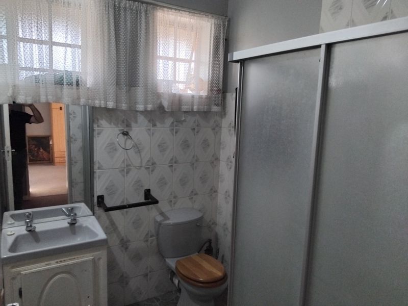 A functional bathroom featuring a shower enclosure, vanity basin, and toilet with dated wall tiling and cabinetry.