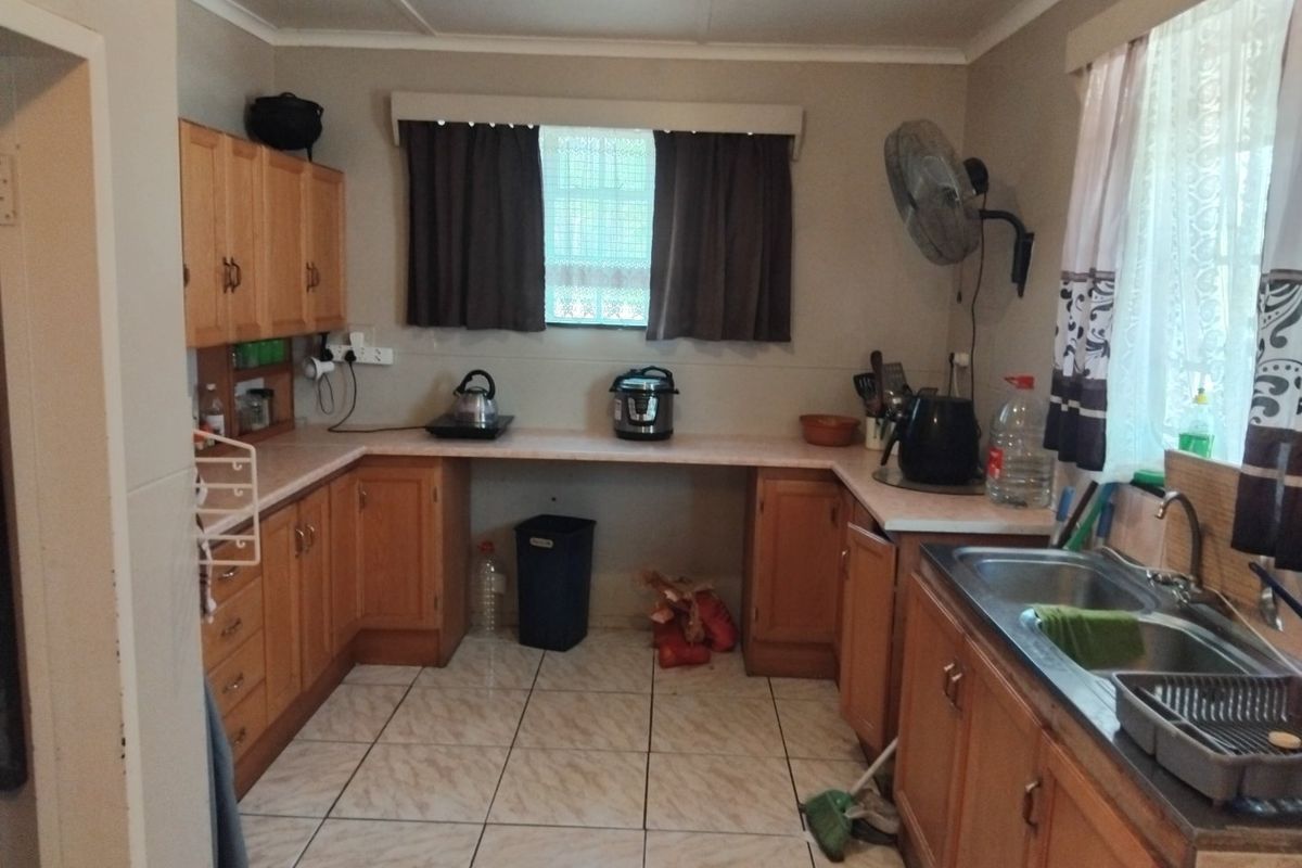 A functional kitchen featuring wooden cabinetry, laminate countertops, and a stainless steel double sink with tiled flooring.