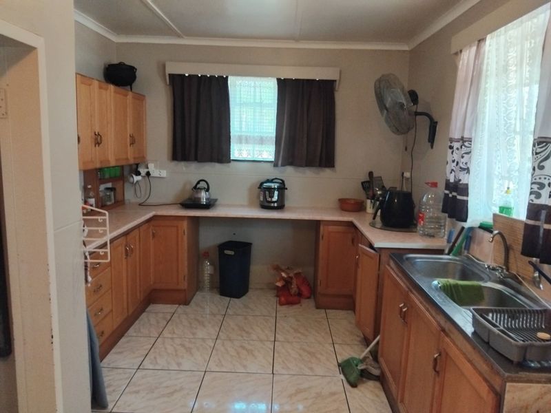 A functional kitchen featuring wooden cabinetry, laminate countertops, and a stainless steel double sink with tiled flooring.