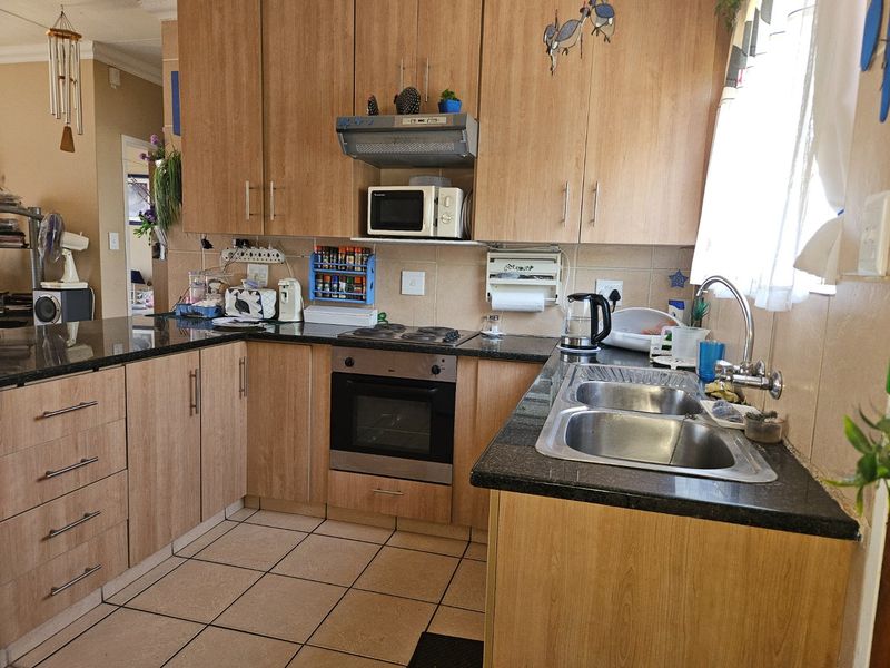 Functional kitchen featuring laminate cabinetry, granite countertops, built-in oven, electric hob, and a stainless steel double sink with tiled flooring.