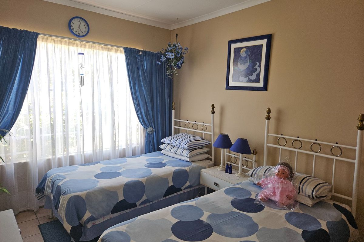 A functional bedroom featuring tiled flooring, coved ceilings, and large windows with curtain rails, providing a comfortable space for two beds.