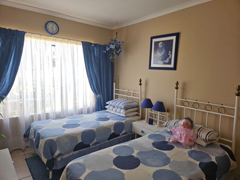 A functional bedroom featuring tiled flooring, coved ceilings, and large windows with curtain rails, providing a comfortable space for two beds.