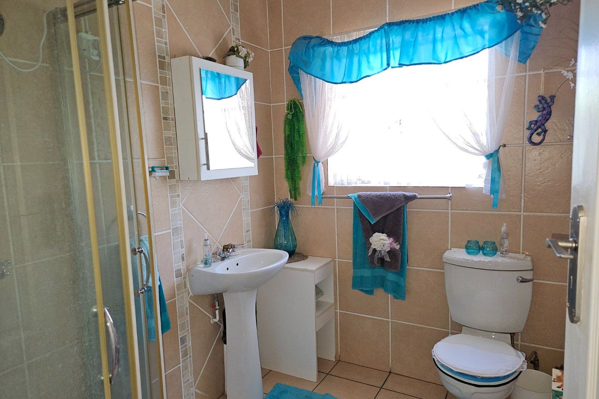 A functional bathroom featuring a pedestal basin, shower enclosure, and toilet with neutral wall and floor tiling.
