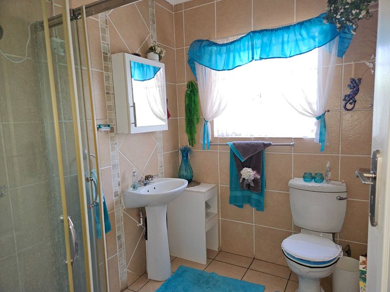 A functional bathroom featuring a pedestal basin, shower enclosure, and toilet with neutral wall and floor tiling.